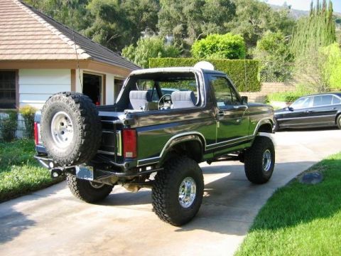 1985 Ford Bronco - This lifted Ford Bronco is parked in a driveway with a house and trees in the background.