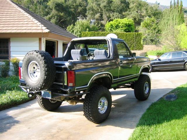 Black lifted Ford Bronco, top off, on driveway, rear 3/4 view