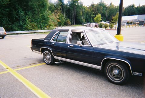 1990 Ford Crown Victoria LTD - Dark blue 1990 Ford Crown Victoria LTD parked in a lot with trees and a building in the background.