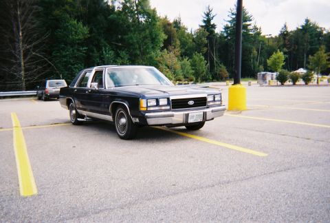 1990 Ford Crown Victoria LTD - A dark blue Ford Crown Victoria is parked in a lot with yellow lines on the asphalt.
