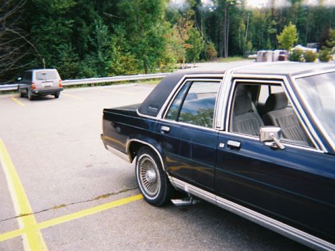 1990 Ford Crown Victoria LTD - A dark blue 1990 Ford Crown Victoria LTD is parked in a lot, with another vehicle visible in the background.
