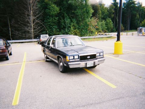 1990 Ford Crown Victoria LTD - A 1990 Ford Crown Victoria LTD is parked in a lot, with other vehicles visible in the background.