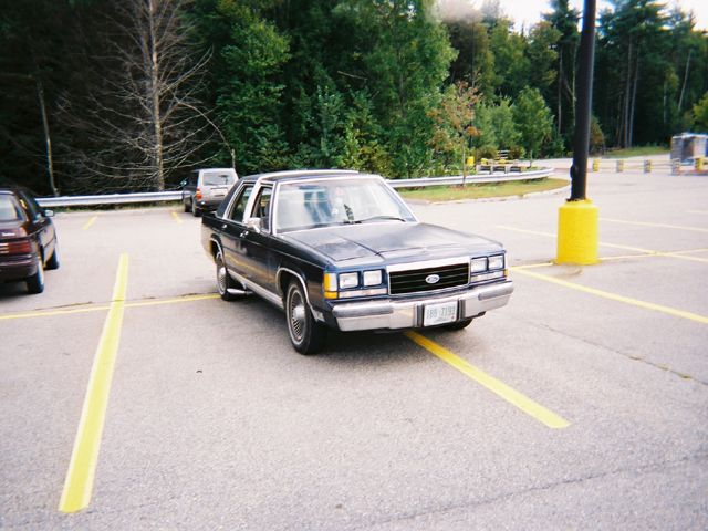 Dark blue 1990 Ford Crown Victoria LTD sedan parked at a 3q-front angle in a parking lot, showing its chrome grille and bumper