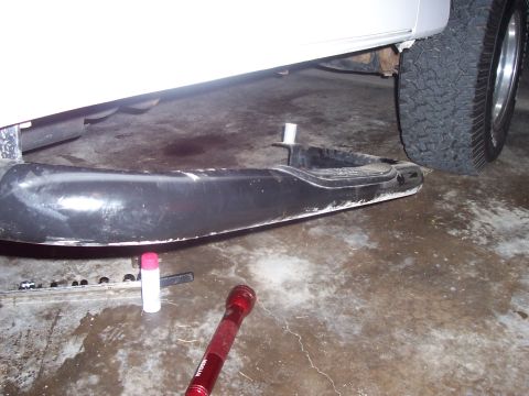 1994 Ford Bronco - A removed black running board lies on a wet garage floor next to the tire of a white vehicle.