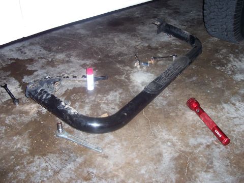 1994 Ford Bronco - A black rocker panel slider, likely for an SUV, lies on a garage floor with tools and a flashlight nearby.