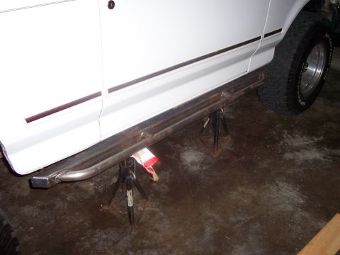 1994 Ford Bronco - The side of a white SUV is shown, supported by jack stands, with custom tubular steps mounted below the doors.