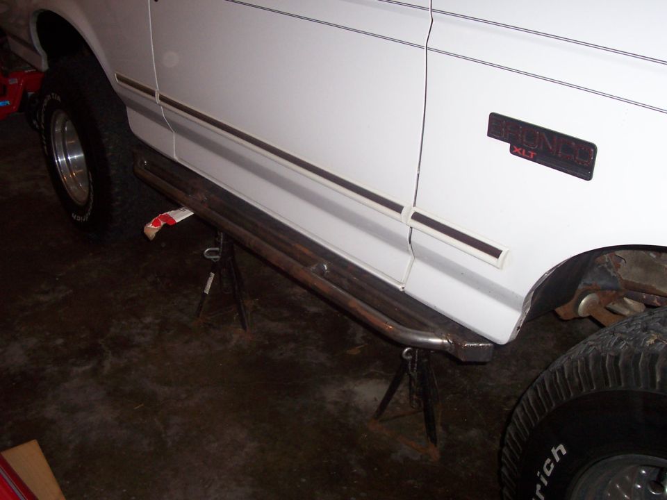 Bare steel rock slider test-fitted to rocker of white Ford Bronco on jack stands
