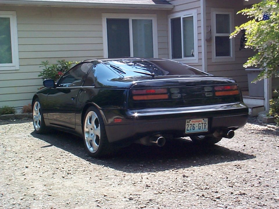 Black Nissan 300ZX coupe from rear 3/4 angle parked on gravel by a house