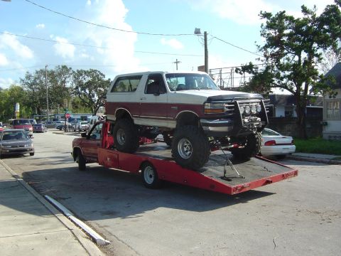 1993 Ford Bronco - A lifted 1993 Ford Bronco is transported on a red flatbed tow truck, a prominent bull bar and two-tone paint scheme.
