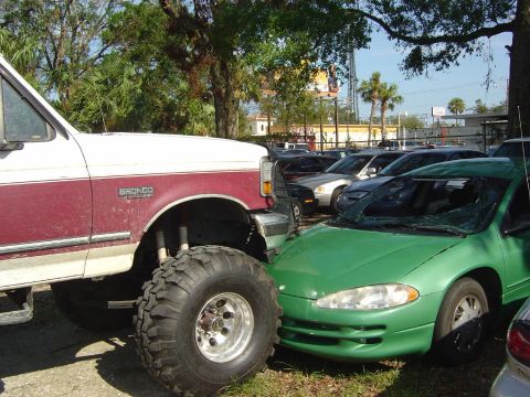 1993 Ford Bronco - A lifted 1993 Ford Bronco is parked very close to a green car that has a shattered windshield.