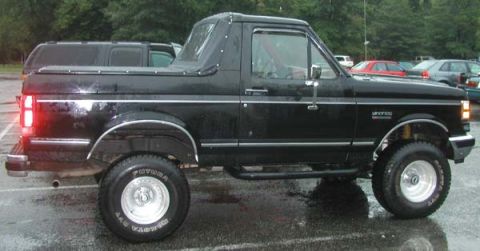 1988 Ford Bronco - This black Ford Bronco, likely a 1987 model, is viewed from the side with a soft top and chrome accents.