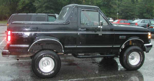 Black Ford Bronco with a soft top, side view, showing chrome trim and aftermarket wheels
