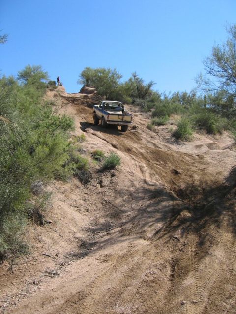1979 Ford Bronco - Wide shot looking up a steep rutted dirt hill climb in the desert, with a topless cream and dark two-tone Ford Bronco perched near the cres…