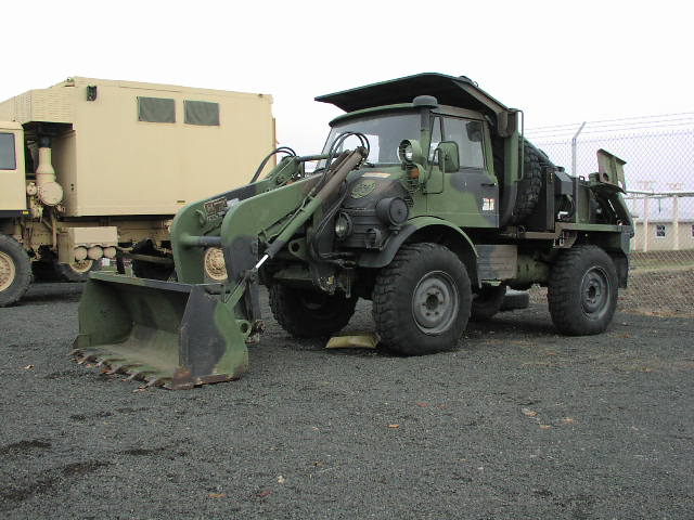 Green military front loader with camouflage paint, parked next to a tan vehicle