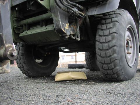 1981 Ford Bronco - The underside of a military vehicle is visible, with large off-road tires and heavy-duty suspension components.