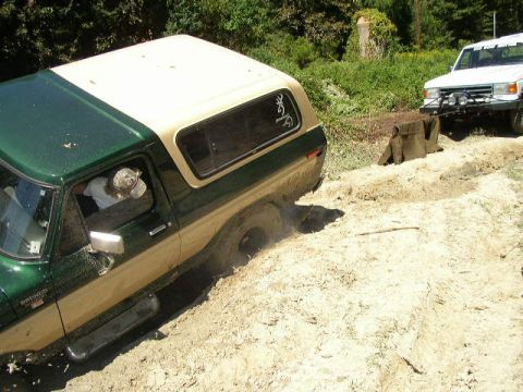 1995 Ford Bronco - A two-tone Ford Bronco struggles in the mud, with a white truck nearby.