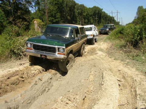 1995 Ford Bronco - A convoy of SUVs navigates a muddy off-road trail under a clear blue sky.