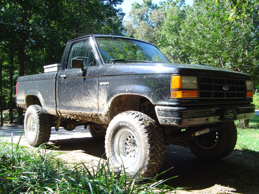 Mud-splattered black 1989 Ford Ranger pickup truck with lifted suspension and off-road tires parked outdoors
