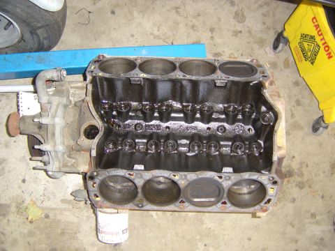 1993 Ford Bronco - Overhead view of a V8 engine block sitting on a garage floor with both cylinder heads removed, showing all eight bores, head gaskets on the…