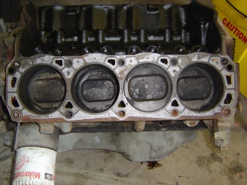 1993 Ford Bronco - Close-up of one bank of a disassembled V8 engine block with the cylinder head removed, showing four carbon-stained cylinder bores, the used…