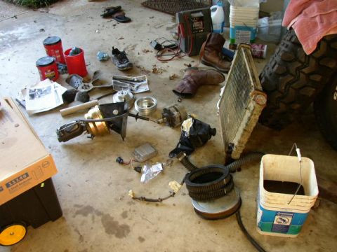 1995 Ford Bronco - Various vehicle parts are scattered on a concrete floor, including a radiator, alternator, brake booster, and air filter.