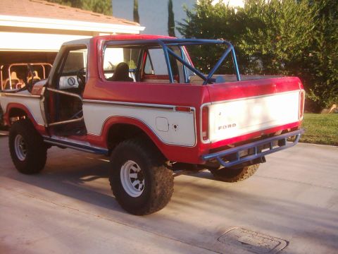 1978 Ford Bronco - This red and white 1978 Ford Bronco features a prominent blue roll cage and an aftermarket rear bumper.