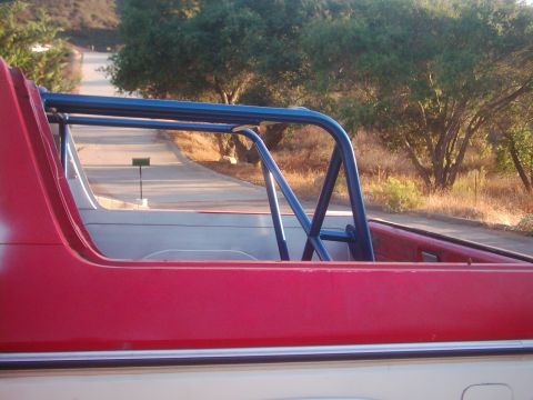 1978 Ford Bronco - The interior roll cage of a red and white vehicle is visible from the rear passenger side, with a road in the background.