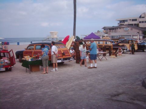 1978 Ford Bronco - A beach scene a woodie station wagon, surfboards, and other vehicles, possibly at a car show or gathering.