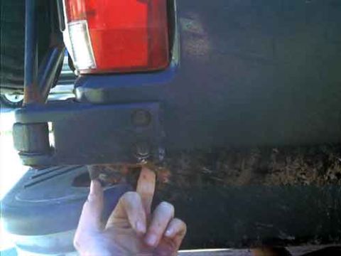 1995 Ford Bronco - Close-up of the rear corner of a dark SUV, showing the red taillight lens above a bracket-mounted rear bumper bolted to the body with two b…
