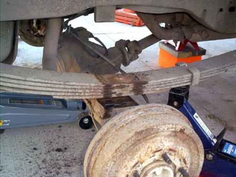 1995 Ford Bronco - Underside view of a rear leaf-spring suspension during a lift install, with the multi-leaf pack, U-bolt plate and axle tube in frame and a…