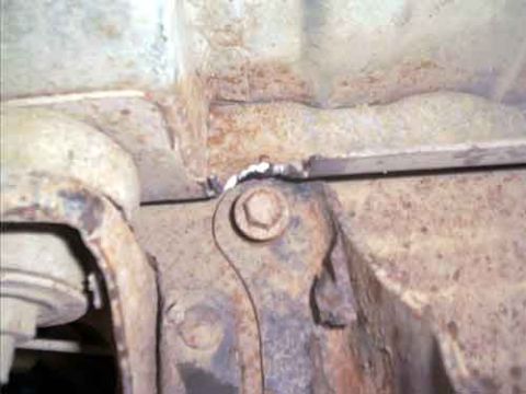 1995 Ford Bronco - Close-up underneath a vehicle of a rusty frame bracket and mount with a fresh weld bead and a hex bolt, a reinforcement typical of a lift o…