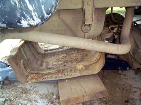 1995 Ford Bronco - Underbody shot of a dust-covered truck showing a rusty rear fuel tank and its mounting straps, with the exhaust pipe running past and a blu…