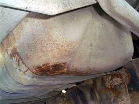 1995 Ford Bronco - Close-up from below a vehicle of the dusty, rounded underside of a metal tank or pan, with rust staining concentrated along its lower seam.