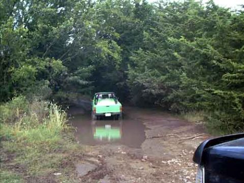 1995 Ford Bronco - A green pickup truck navigates a muddy path through a wooded area.
