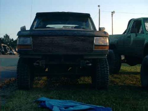 1995 Ford Bronco - A dark Ford Bronco is parked in front of a green truck under a clear sky.