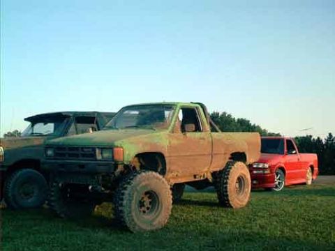 1995 Ford Bronco - A lifted green pickup truck sits in a grassy field next to a red pickup truck under a clear sky.