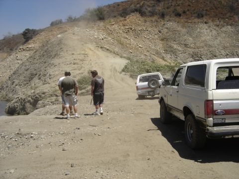 1990 Ford Bronco - Two men pause on a dusty hillside trail beside a white Ford Bronco and a parked SUV ahead.