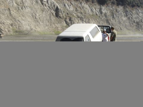 1990 Ford Bronco - white SUV sits on a dusty trail at the base of a rocky slope while two people stand beside the open driver's door.