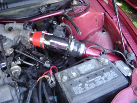 1998 Ford Taurus - Close-up of a car's engine bay, showing an aftermarket cold air intake system and the battery.