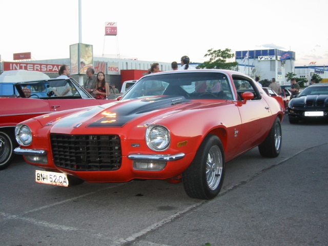Red 1970s Chevrolet Camaro with black stripes on hood, parked outside