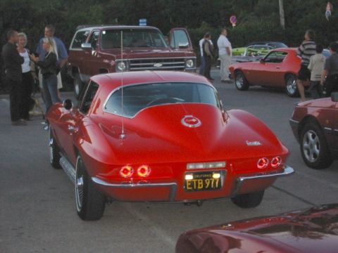 1992 Ford Crown Victoria - A red 1965 Chevrolet Corvette Sting Ray coupe is parked at an outdoor gathering with other vehicles and people.