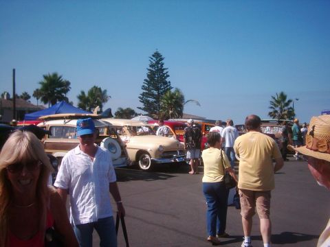 1978 Ford Bronco - Vintage station wagon with surfboards on roof at an outdoor car show. Multiple vehicles and people are present.