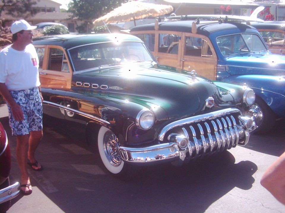 Green woody wagon with chrome grille and whitewall tires, parked next to a blue car