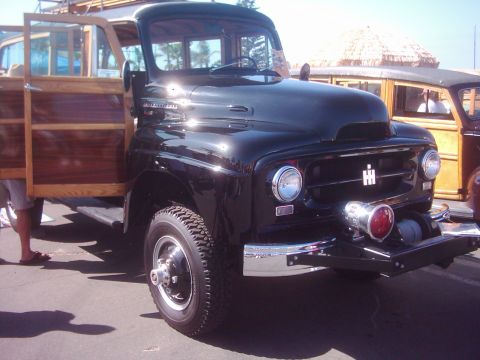 1978 Ford Bronco - A black International Harvester truck with wood paneling and an open door is parked next to another woody vehicle.
