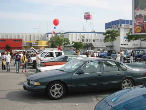 1992 Ford Crown Victoria - A dark green sedan is parked in a lot with other vehicles and people milling around.