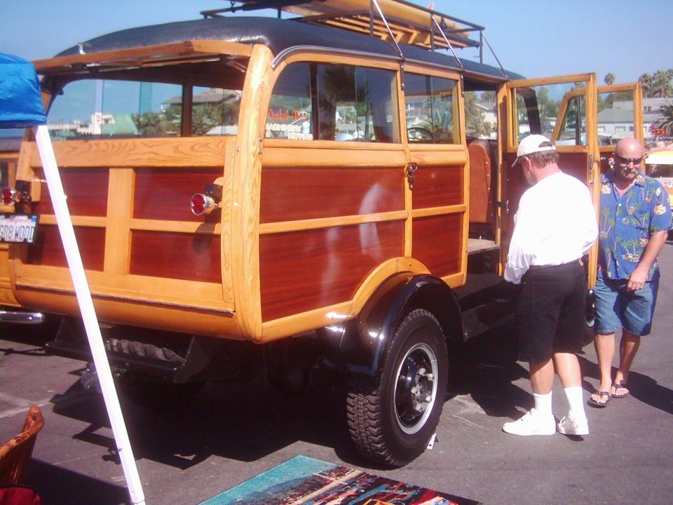 Woodie station wagon with surfboard on roof rack, two men standing nearby