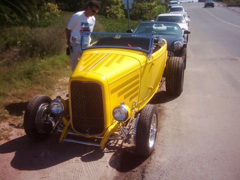 1978 Ford Bronco - A bright yellow hot rod roadster is parked on the side of a road, with other vehicles in the background.
