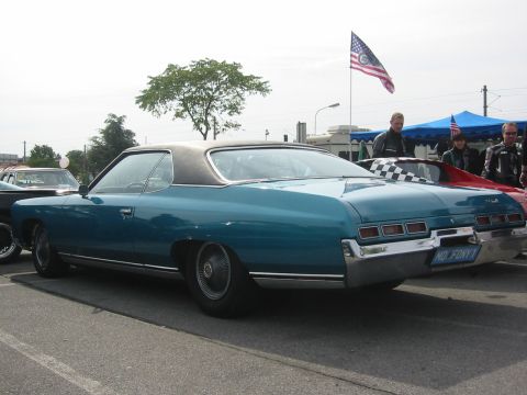 1992 Ford Crown Victoria - Rear view of a teal 1971 Chevrolet Caprice coupe, parked at an outdoor event with an American flag flying.