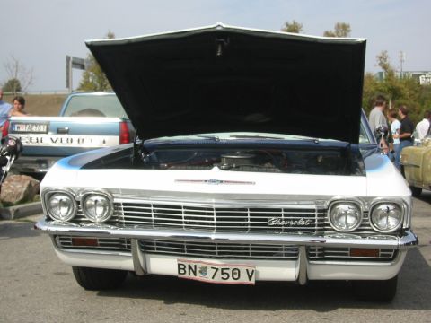 1992 Ford Crown Victoria - A white 1965 Chevrolet Impala is displayed with its hood open, revealing the engine compartment.