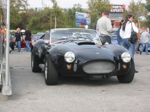 1992 Ford Crown Victoria - A black AC Cobra replica is parked outdoors with people around it and buildings in the background.